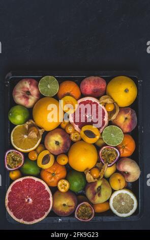 Variety of tropical colorful summer fruits on black background with copy space, some of the citrus fruits cut in half Stock Photo