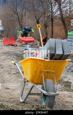 Concrete curb blocks lie inside a construction wheelbarrow against the backdrop of a workplace in blur. Stock Photo