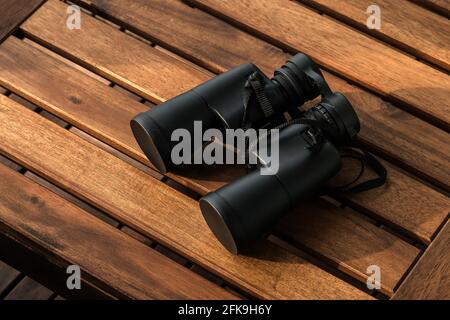Black binoculars on a brown wooden table background with copy space Stock Photo