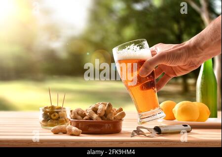 Man having a snack in the countryside with a glass of beer in hand and a table full of snacks Stock Photo