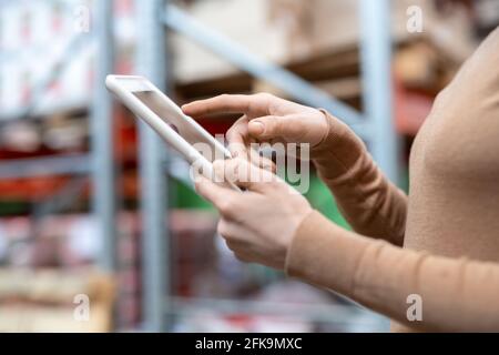 Close-up of unrecognizable warehouse manager in sweater checking goods positions on tablet while working with data Stock Photo