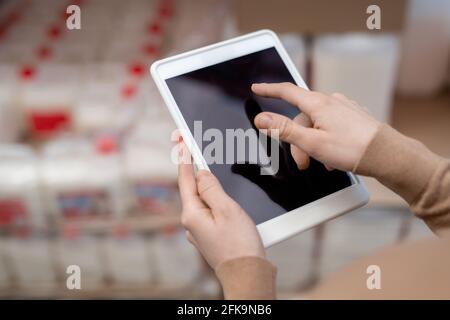 Close-up of unrecognizable manager using gadget while doing inventory of products at warehouse Stock Photo