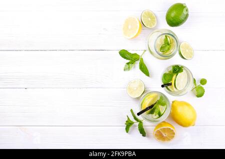 Vintage bottle with two glasses of refreshing non alcoholic mojito lemonade, sparkling water drink with lemon, lime slices, mint leaves, straw, wooden Stock Photo