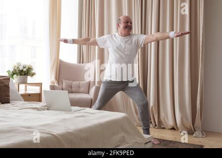 Elderly man practicing yoga warrior asana. Positive mood on sports activities. standing asana of yoga Stock Photo