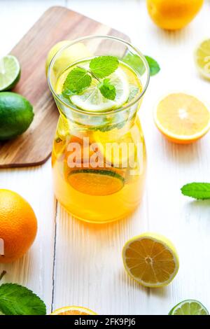 Iced lemonade pitcher & two glasses, wooden juicer, cold citrus infused water, lemon & lime, mint leaves, cutting board on white wooden windowsill. Ap Stock Photo