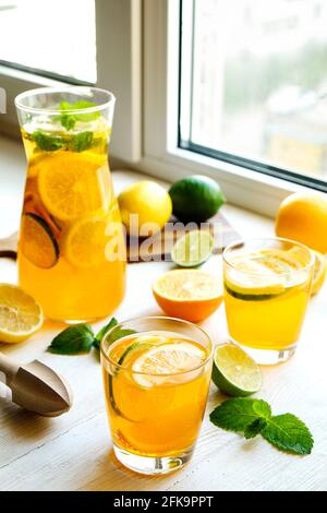 Iced lemonade pitcher & two glasses, wooden juicer, cold citrus infused water, lemon & lime, mint leaves, cutting board on white wooden windowsill. Ap Stock Photo