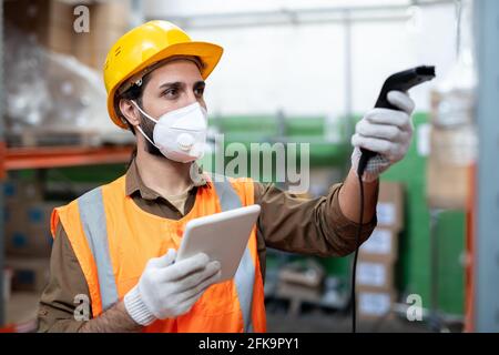 Busy mixed race warehouse employee in facial mask and gloves using digital tablet while scanning code of item Stock Photo