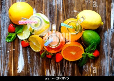 Three vintage bottles of fresh ice cold lemonade, different taste drinks w/ lemon, orange, grapefruit, lime, mint leaves & strawberry on grunged woode Stock Photo