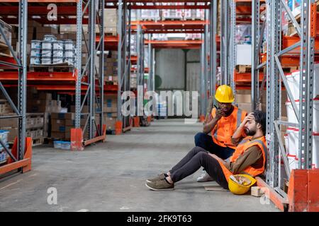 African-American man in work helmet calling ambulance for warehouse colleague feeling headache Stock Photo