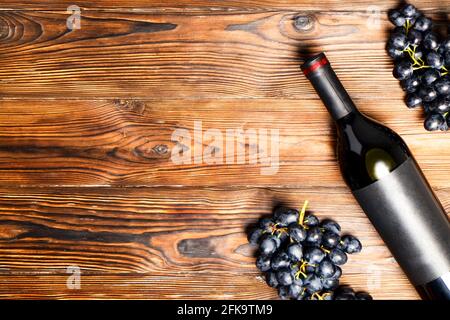 Unopened vintage bottle of red wine with blank matte black label & bunches of ripe grapes on wooden table background. Expensive bottle of cabernet sau Stock Photo