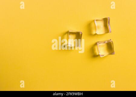 Flat lay of a yellow surface where there are some transparent plastic cubes with side light and copy space Stock Photo