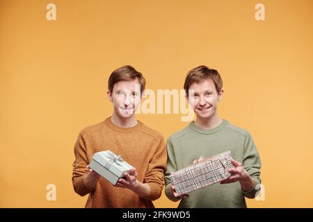 Portrait of happy handsome young twins standing with packed gift boxes against orange background Stock Photo