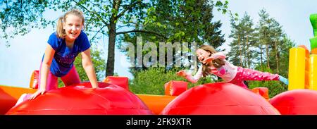 Two happy little girls having lots of fun while jumping from ball to ball on an inflate castle. Stock Photo