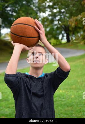 Young teen boy focuses on the goal.  He is practicing basketball in his backyard.  He is concentrating on making his shot. Stock Photo