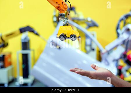 Close-up industrial robotic gripping yellow toy car send to hand human on blurred smart factory background, industry 4.0 and iot technology concepะ Stock Photo