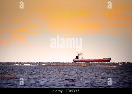 The cargo ship moves along the narrow fairways and swans sit in the shallow waters of the bay. High clouds illuminated by the sun Stock Photo