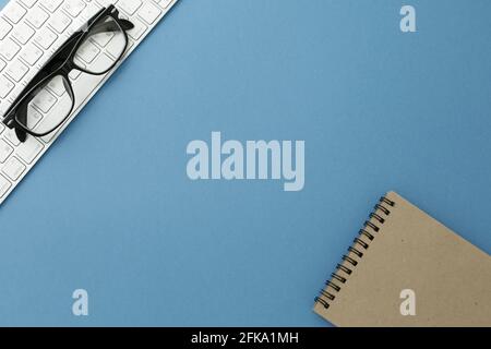 Glasses notpad and keyboard on blue background. Close-up Stock Photo