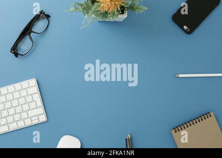 Glasses white keyboard flower notepad mouse pen pencil and phone on blue background Stock Photo