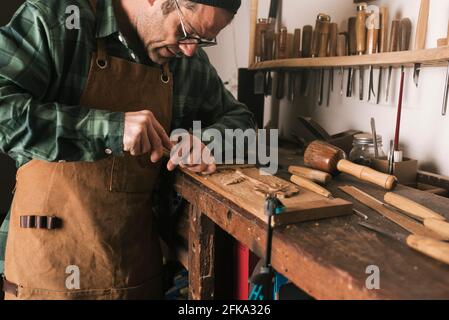 Side shot of a cabinetmaker working on a wood carving with a chisel. Stock Photo