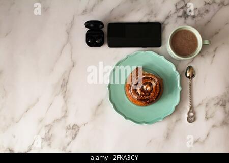 A plate with a bun, a cup of coffee and gadgets on the table. Stock Photo