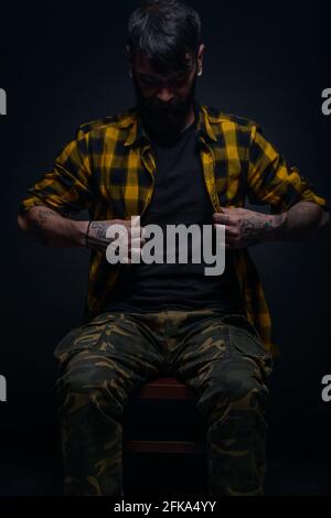 Bearded man with tattoos on his hands and neck wearing yellow black shirt and army pants Stock Photo