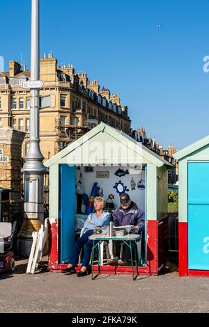 A Senior Couple Sitting Outside Their Beach Hut On Hove Seafront, Brighton, East Sussex, UK. Stock Photo