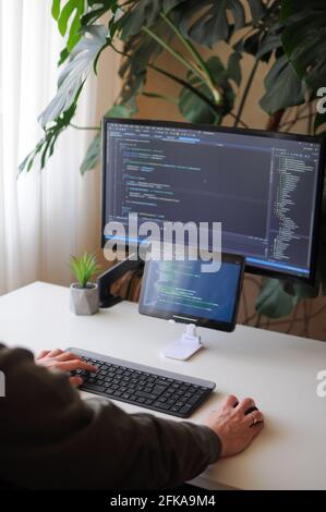 Developer is coding using screen and tablet. Freelancer is working from home Stock Photo
