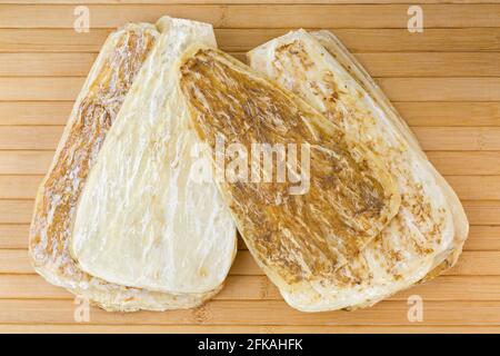Closeup of dried Dong quai, Dang Gui, known as female ginseng, flattened root on wooden mat background (Angelica sinensis) Stock Photo