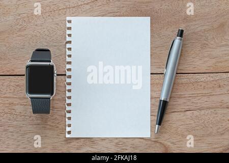 Smart watch with leather bands, blank white paper from spiral ring notebook and a silver pen on wooden background Stock Photo