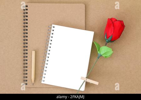 Top view of blank notebook on natural brown paper next to wooden pencil and red rose Stock Photo
