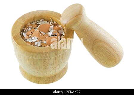 Crushed Chicken egg shells inside wooden mortar next to pestle, isolated on white background. Stock Photo