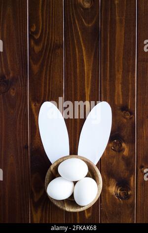 Easter eggs in wooden bowl on wood with bunny ears and copy space; Easter bunny abstract; holiday Stock Photo