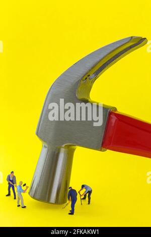 Steel claw hammer with red handle on yellow background with small mini miniature worker men working nearby Stock Photo