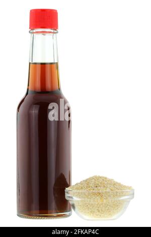 A bottle of cold pressed Sesame oil next to a bowl of white Sesame seeds, isolated on white background Stock Photo