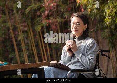 A lonely old woman in the yard in the sun Stock Photo