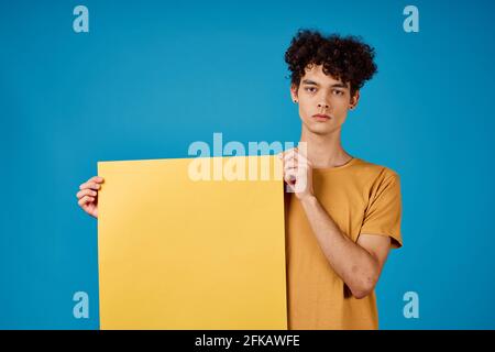 guy with curly hair yellow posters in hands Copy Space blue background studio Stock Photo