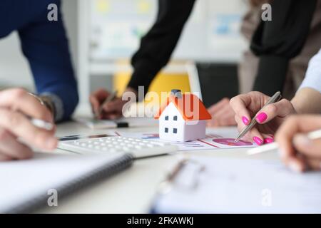 Group of people discussing chart on documents near toy house closeup Stock Photo