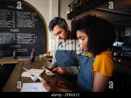 Mixed race colleagues looking at paper work holding digital tablet managing bank statements for trendy coffee shop Stock Photo