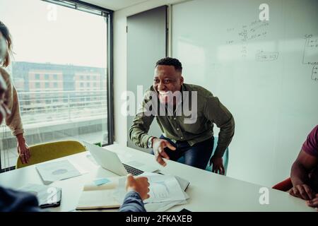 Mixed race business man laughing with colleagues discussing project plans in board room during team meeting  Stock Photo