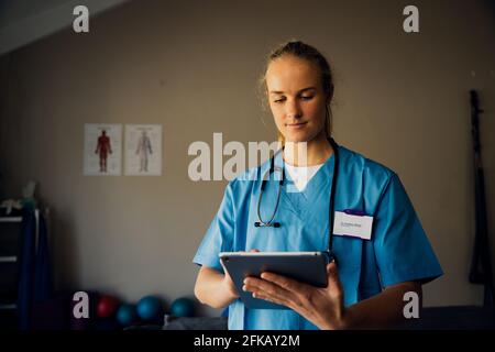 Caucasian nurse preparing for online consultation with sick patient using digital tablet standing in clinic  Stock Photo