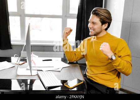 Happy young businessman having an online meeting with coworkers, hearing good news about project, enjoying results of teamwork. Excited male Stock Photo