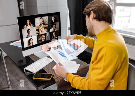 Concentrated male employee in yellow shirt working from home, having online briefing meeting with colleagues. Serious young businessman doing Stock Photo