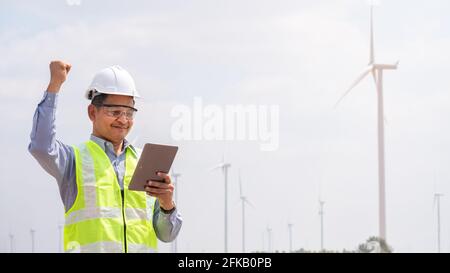 Successful engineer windmills using tablet with wind turbine in background Stock Photo