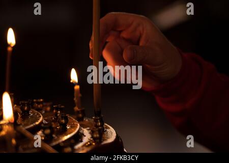 Batumi, Georgia - March 15, 2021: Woman's hand in a red jacket puts a church candle Stock Photo
