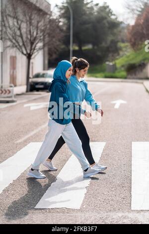 Cheerful active girls wearing sports clothes walking and crossing the street in zebra crossing Stock Photo Alamy