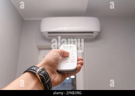Close-up of a man's hand with a wristwatch holding a remote control in front of an air conditioner, copy space Stock Photo
