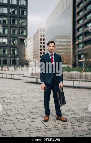 Confident businessman with briefcase standing in office park Stock Photo
