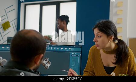 Mechanical engineers using computer, discussing about manufacturing new project, taking notes on clipboard. Man technician working at pc, screen shows 3D engine made with CAD software. Stock Photo