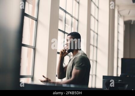 Smiling businessman talking on smart phone by window at creative office Stock Photo