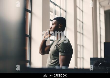 Male entrepreneur talking on mobile phone while looking through window in office Stock Photo